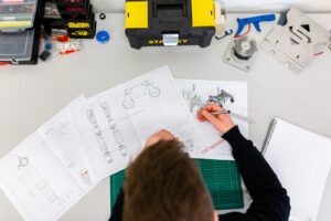 A person using a caliper to measure technical engineering drawings on a desk
